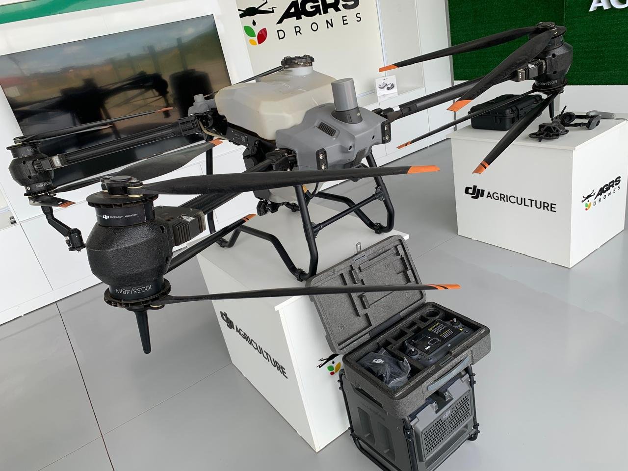 Drone pulverizador DJI Agras exposto ao lado do case do controle e da estação, em showroom da AGRS Drones
